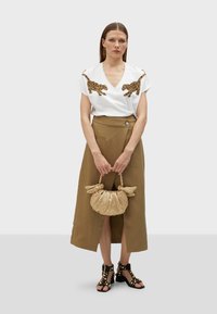 T-shirt bianco con scollo a V e ricamo di leopardo dorato, abbinato a una gonna A-line marrone, sandali neri con borchie e una borsa beige testurizzata.