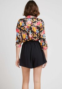 Blouse florale avec un fond noir, ornée de fleurs jaunes, roses et bleues vives, associée à un short noir, pour un look décontracté.