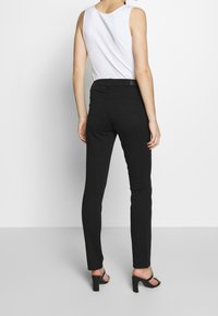 Jeans negros ajustados de tiro medio, con bolsillos traseros y una textura suave, combinados con una blusa sin mangas blanca.