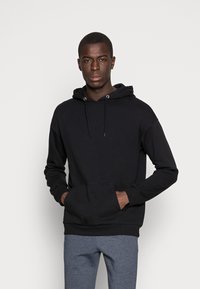 Svart hoodie med ficka framtill, dragsko och ribbad mudd. Bärs med grå träningsbyxor som har en slät yta.