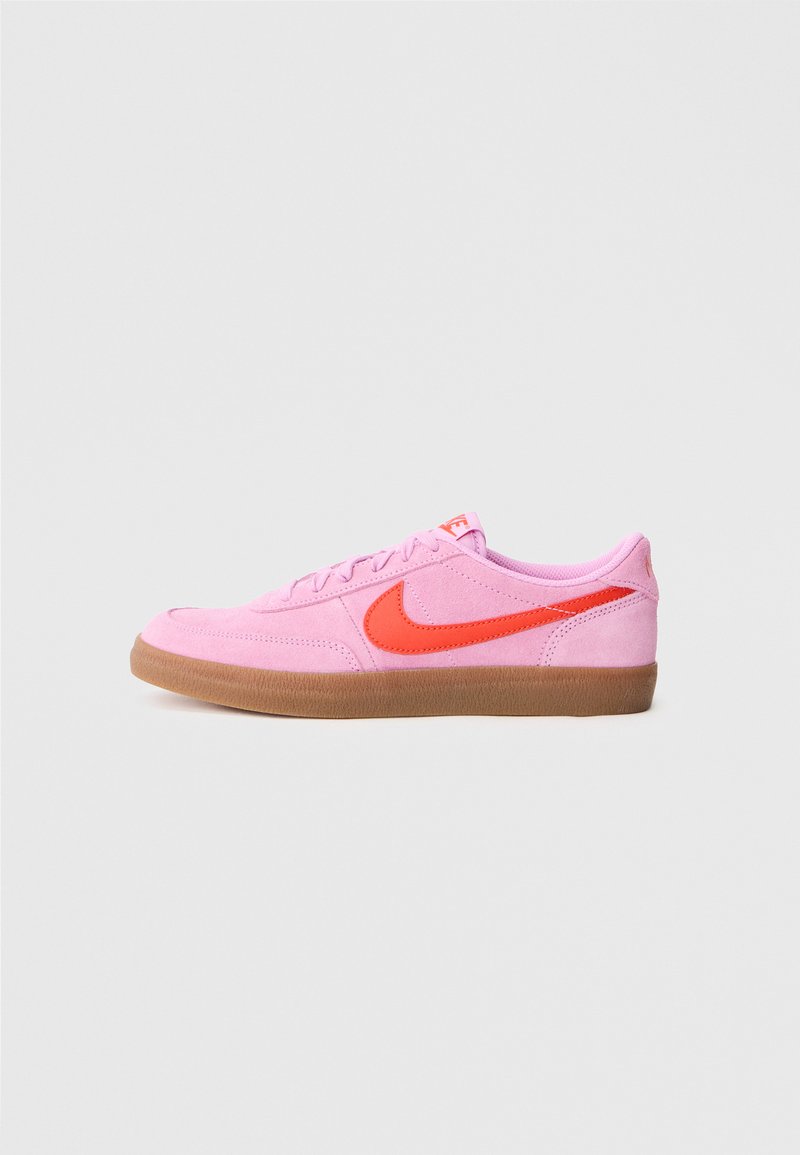 Rožinės zomšos sportbačiai su oranžiniu swoosh logo, virvelių dizainas ir gumos guminis padas. Lygi tekstūra ir suapvalinta nosies forma.