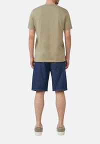 Oliwkowa koszulka z krótkim rękawem połączona z ciemnogranatowymi szortami dżinsowymi. Strój charakteryzuje się luźnym krojem i jest uzupełniony jasnoszarymi trampkami.