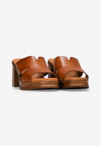 Sandalias de piel marrón con tacón bloque, con diseño calado y punta abierta, que presentan una textura suave y una plantilla acolchada en tono marrón.