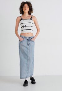 White cropped tank top with black horizontal stripes and bow details, paired with a long light blue denim skirt. Black shoes complete the outfit.
