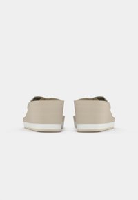 Beige kilehæler sandaler med brede stropper og en teksturert overflate. Plattformen har en hvit stripe nederst for kontrast.