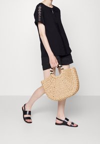 Top nero leggero con dettagli in pizzo, abbinato a pantaloni corti neri, sandali neri e una borsa di paglia intrecciata con manici di perline.