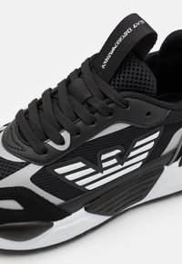 Svart och grå atletisk sneaker med nät- och syntetmaterial, böjd form, framträdande logotyp och mönstrad gummisula.