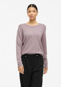 Helllila, gestrickter Pullover mit langen Ärmeln und Rundhalsausschnitt, kombiniert mit schwarzen Hosen mit goldenen Akzenten.