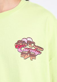 Hellgrünes Baumwoll-T-Shirt mit einem bunten Grafikdruck, der den Text "Air Crew Candy" sowie Eismotiven in rosa und braunen Farbtönen zeigt.