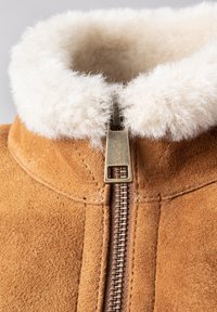Tan suede jacket with a white faux fur collar, featuring a bronze zipper and stitching details along the edges.
