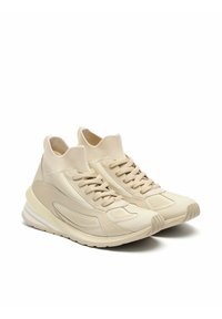 Zapatillas deportivas beige con parte superior tejida y cuello acolchado, que presentan un diseño con cordones, paneles texturizados y suelas de goma para mejor agarre.