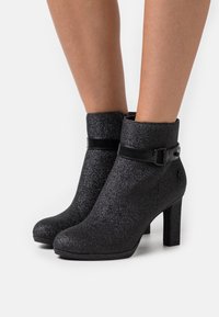 Bottines à paillettes noires avec une texture lisse, dotées d'une boucle décorative et d'un talon haut. Le design est moderne et ajusté.