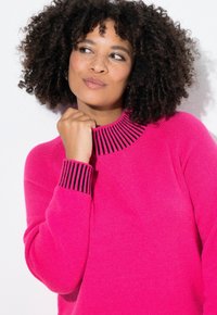 Maglione fucsia con colletto e polsini neri a coste, caratterizzato da una vestibilità ampia e una texture morbida. Lo sfondo è bianco semplice.