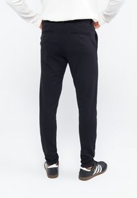 Zwarte broeken met een slim fit, een vlakke voorkant, twee achterzakken en een gladde textuur, gecombineerd met zwart-witte sportschoenen.