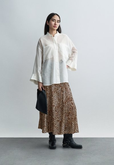 Λευκό πουκάμισο με κουμπιά και δύο τσέπες στο στήθος, συνδυασμένο με φούστα maxi καφέ με λεοπάρ σχέδιο, μαύρα μποτάκια μέχρι τον αστράγαλο και μαύρο τσαντάκι χειρός.