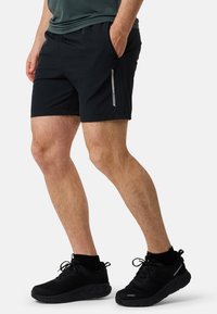 Svarta herrsportshorts med sidofickor, elastisk midja och reflexdetaljer. Bärs med svarta vattentäta sneakers.