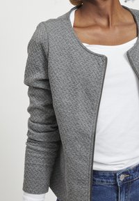 Gray textured jacket with a zip closure and round neckline, worn over a white t-shirt. Featured are rolled cuffs and tailored fit.