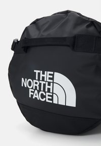 Sac à dos noir en tissu durable, de forme circulaire, avec une bandoulière réglable et un grand logo blanc. Texture lisse avec une finition mate.