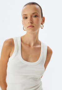 Witte geribbelde tanktop met een ronde halslijn, die een aansluitend ontwerp en een soepele textuur laat zien. Eenvoudige en minimalistische stijl. Gouden oorringen.