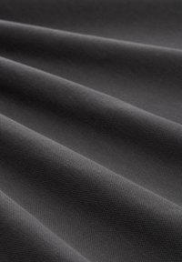 Zbliżenie ciemnoszarego materiału z ukośnymi fałdami i widoczną, drobną fakturą tkaniny.