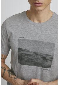 Camiseta de algodón gris con un estampado gráfico de líneas verticales y un paisaje difuminado, con el texto "Perspectiva" y una cita debajo.