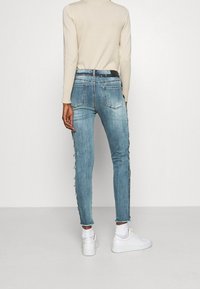 Vaaleansiniset farkut, joissa on kapea istuvuus, rispaantuneet sivusaumat, takataskut ja keskivartalolle istuva vyötärö. Yhdistetty valkoisiin tennareihin.