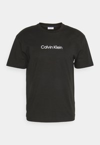 T-shirt noir en coton avec un col ras du cou et des manches courtes, avec le logo "Calvin Klein" imprimé en blanc sur le devant.