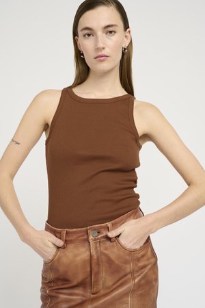 Top in maglia a coste marrone con scollatura rotonda, abbinato a una gonna in pelle a vita alta con tasche frontali e chiusura a bottoni.