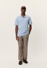 Ανοιχτό μπλε πόλο με κοντά μανίκια και γιακά, συνδυασμένο με ανοιχτό μπεζ παντελόνι. Σκούφο σκούρου καφέ και καφέ παπούτσια ολοκληρώνουν το ντύσιμο.