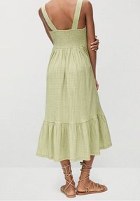 Robe à carreaux verts avec un buste smocké, de larges bretelles et un ourlet évasé. Associée à des sandales gladiateurs beiges.