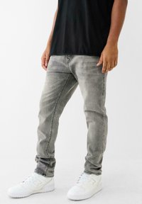 Jeans din denim gri, cu o croială slim, având zone decolorate, detalii cusute și buzunare frontale. Asortate cu adidași albi.