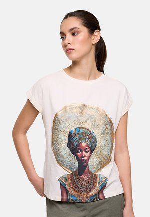 Mujer con cabello oscuro recogido en una coleta, lleva una camiseta blanca que muestra un retrato detallado y colorido de una mujer con vestimenta tradicional africana.