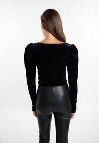 Schwarzes Samtoberteil mit schulterlangen Puffärmeln und weitem Ausschnitt, kombiniert mit schwarzen, hoch taillierten Lederhosen. Einfaches und elegantes Design.
