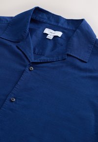 Chemise à manches courtes bleu marine en tissu léger, dotée d'un col classique, d'une fermeture à boutons et d'une surface texturée. Étiquette de la marque visible.