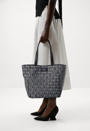 Borsa a tracolla bianca e nera con pois, dotata di manici robusti, realizzata in materiale sintetico. Presenta un'etichetta sul davanti.