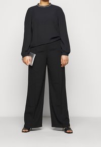 Svart långärmad blus med prydd halsringning, tillsammans med vida svarta byxor. En silverfärgad clutch och svarta sandaler med remmar fulländar looken.