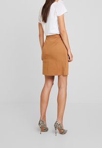 Hnědá texturovaná sukně s přiléhavým střihem, kombinovaná s bílou košili a lodičkami s hadím vzorem. Oblečení se vyznačuje jemným mřížkovaným vzorem.