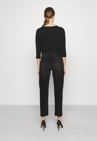 Camisa negra de manga larga con un corte holgado, combinada con jeans oscuros y ajustados que tienen los puños deshilachados, usados con zapatos de tacón alto negros.