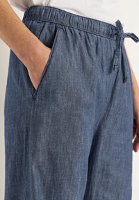 Blå chambraybyxor med elastiskt midjeband och snörning, som har sidofickor och en avslappnad passform med en slät textur.