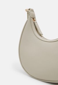 Jasnoszara skórzana torebka o zaokrąglonym kształcie, wyposażona w zamek błyskawiczny i złociste akcenty metalowe. Gładka faktura i czyste linie.