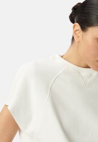 Sudadera blanca de manga corta hecha de una tela suave, con cuello redondo y mangas raglán, con un diseño limpio y minimalista.