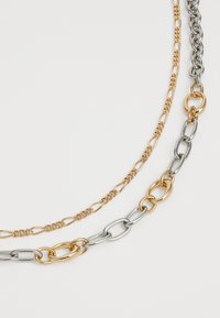 Due collane con maglie alternate di catena dorata e argentata, una con maglie d'oro fine e l'altra con maglie di metallo misto più grandi su uno sfondo bianco.