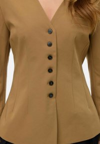 Blazer ajusté marron avec un col en V, six boutons noirs, silhouette cintrée et délicates pinces. Tissu lisse avec une finition mate.