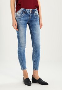 Jeans skinny de mezclilla en azul claro, con un acabado desgastado, ligeros desgastes y diseño de cinco bolsillos con cierre de doble botón.