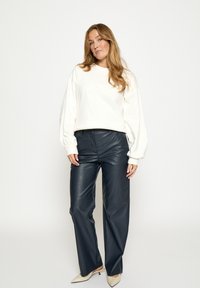 Witte, losvallende trui met verlaagde schouders gecombineerd met hooggetailleerde, donkerblauwe lederen broek en beige pumps met spitse neus.