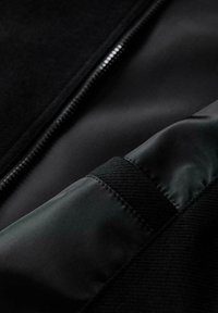 Czarna kurtka z gładką satynową podszewką, teksturowanym materiałem na zewnątrz i metalowym zamkiem błyskawicznym wzdłuż jednego boku.