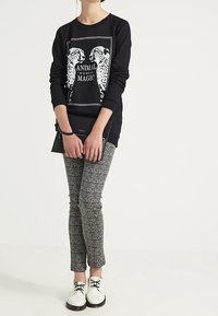 Sudadera negra con un gráfico de guepardo y el texto "MAGIA ANIMAL", combinada con pantalones grises texturizados y zapatos blancos con cordones.