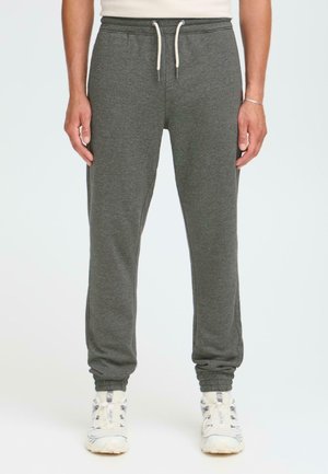 Gray jogger pants made of soft fabric, featuring an elastic waistband with drawstring, cuffed ankles, and side pockets. Mounted on white sneakers.