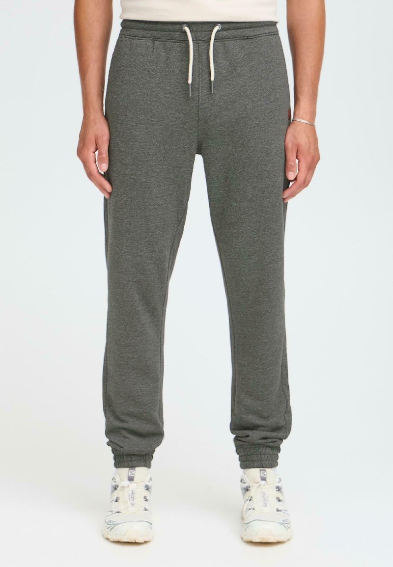 Graue Jogginghosen aus weichem Stoff, mit einem elastischen Bund und Kordelzug, schmalen Knöcheln und seitlichen Taschen. Kombiniert mit weißen Sneakers.