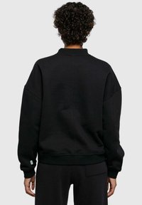 Svart genser med rund hals, senkede skuldre, ribbestrikkede mansjetter og en avslappet passform, laget av myk bomull, med en teksturert overflate.